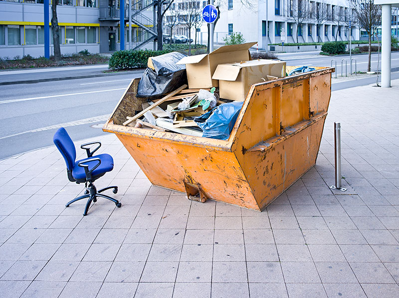 Befüllter Container am Straßenrand. Daneben ein Schreibtischstuhl.