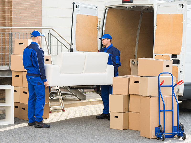 Zwei Männer in Arbeitskleidung tragen eine Couch.