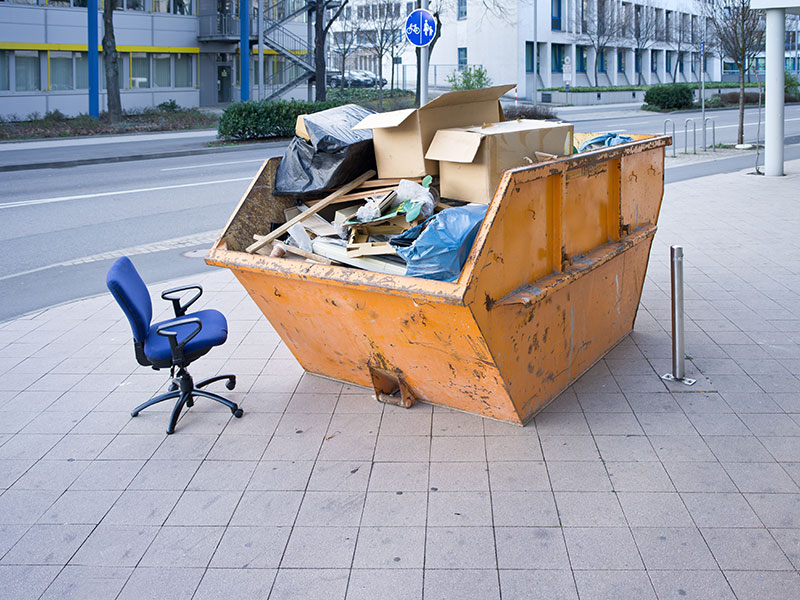 Befüllter Container am Straßenrand. Daneben steht ein Schreibtischstuhl.